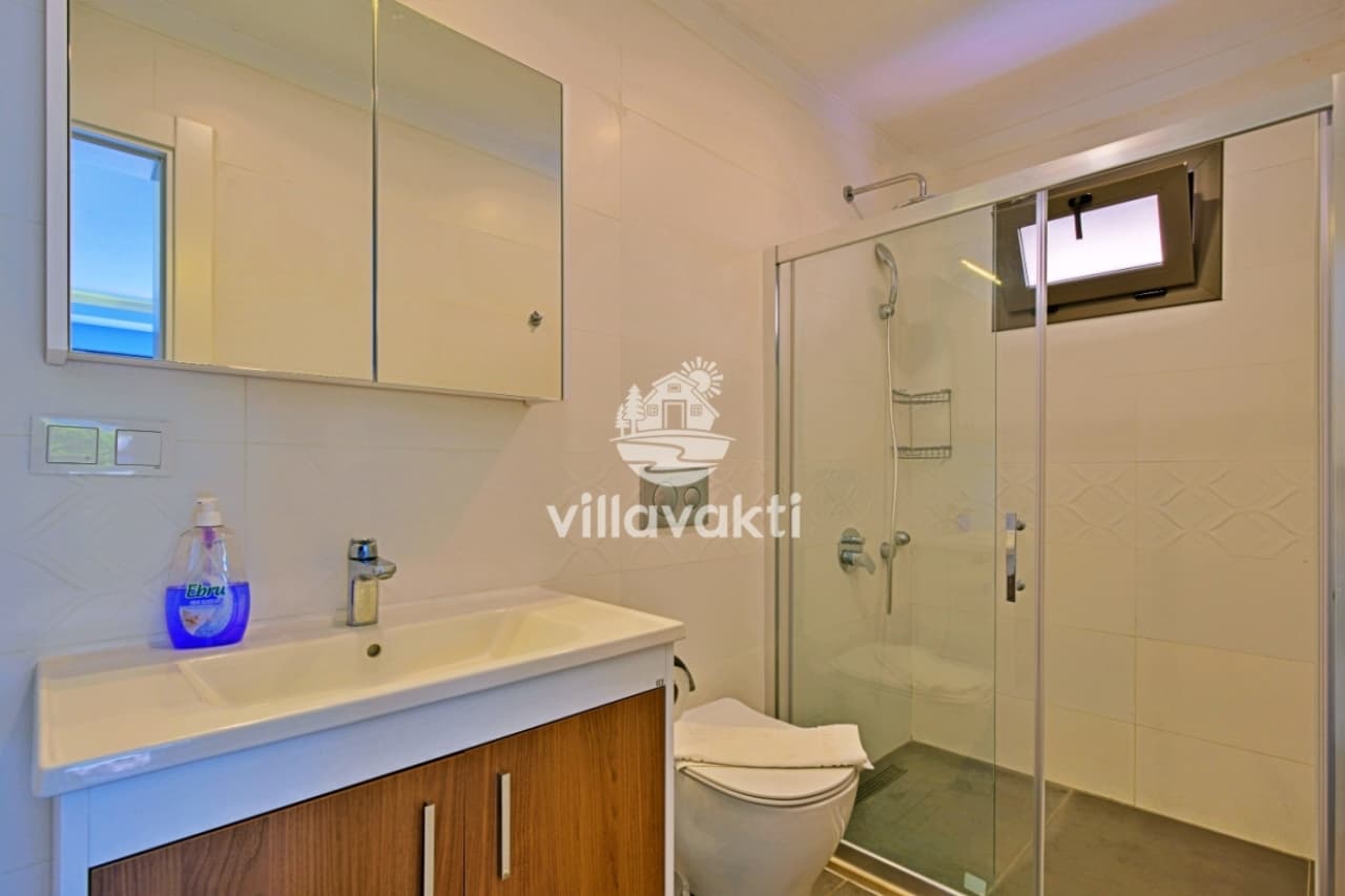 Beyaz lavabo dolabı, cam duş kabini ve klozet bulunan banyo.