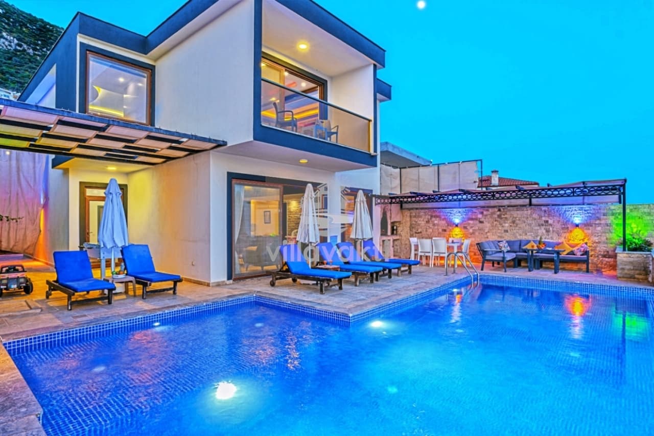 Aydınlatmalı havuzu ve şezlongları olan, taş duvarlı veranda ve modern villa.