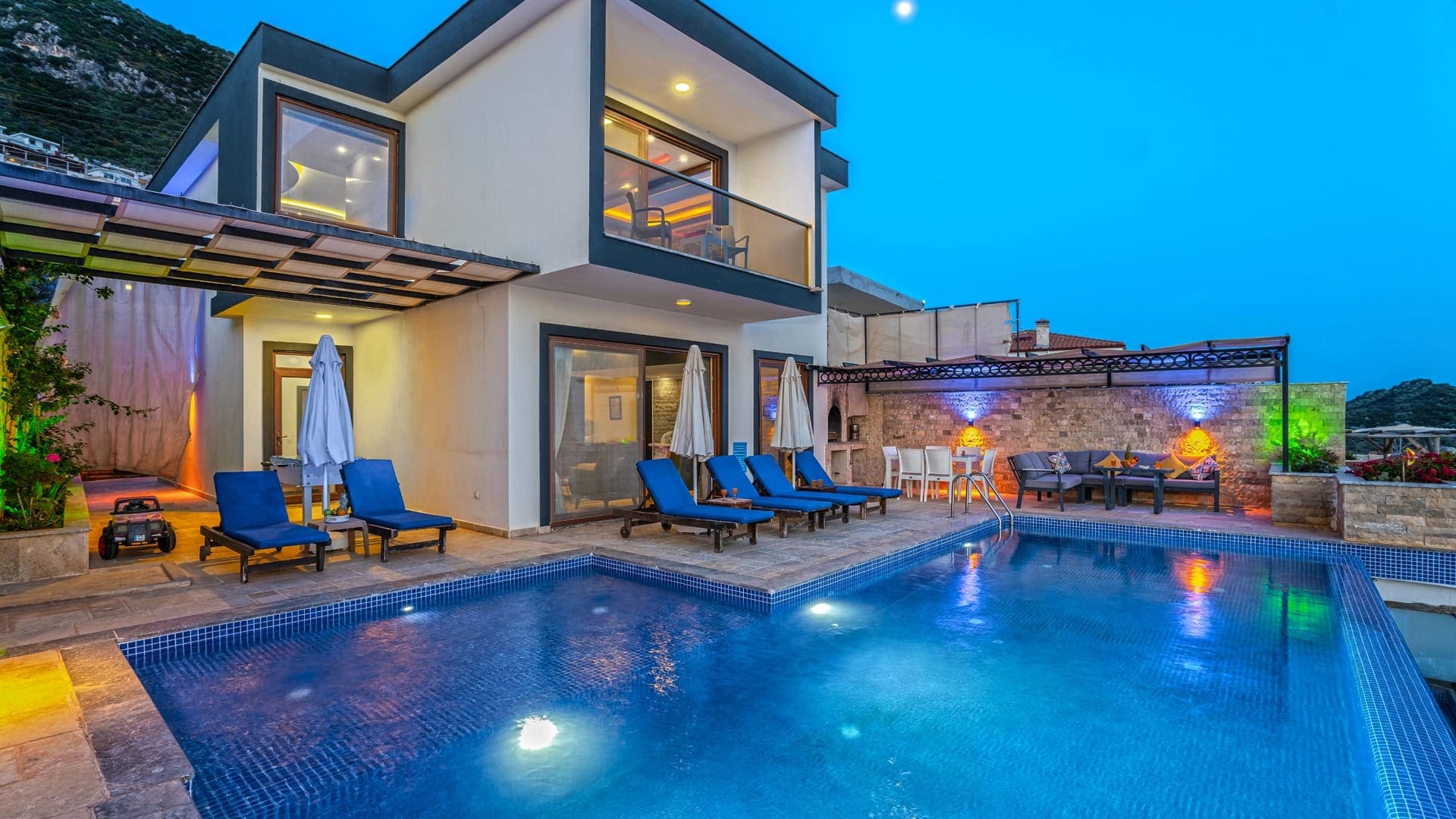 Akşam ışıklandırmalı yüzme havuzu ve şezlongları bulunan modern villa.