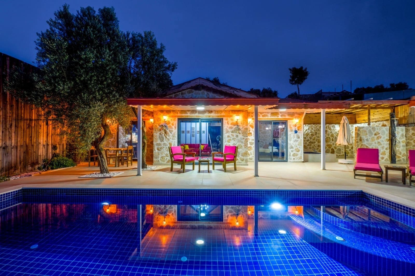 Akşam ışıklandırmalı havuz başı ve taş villa verandası.