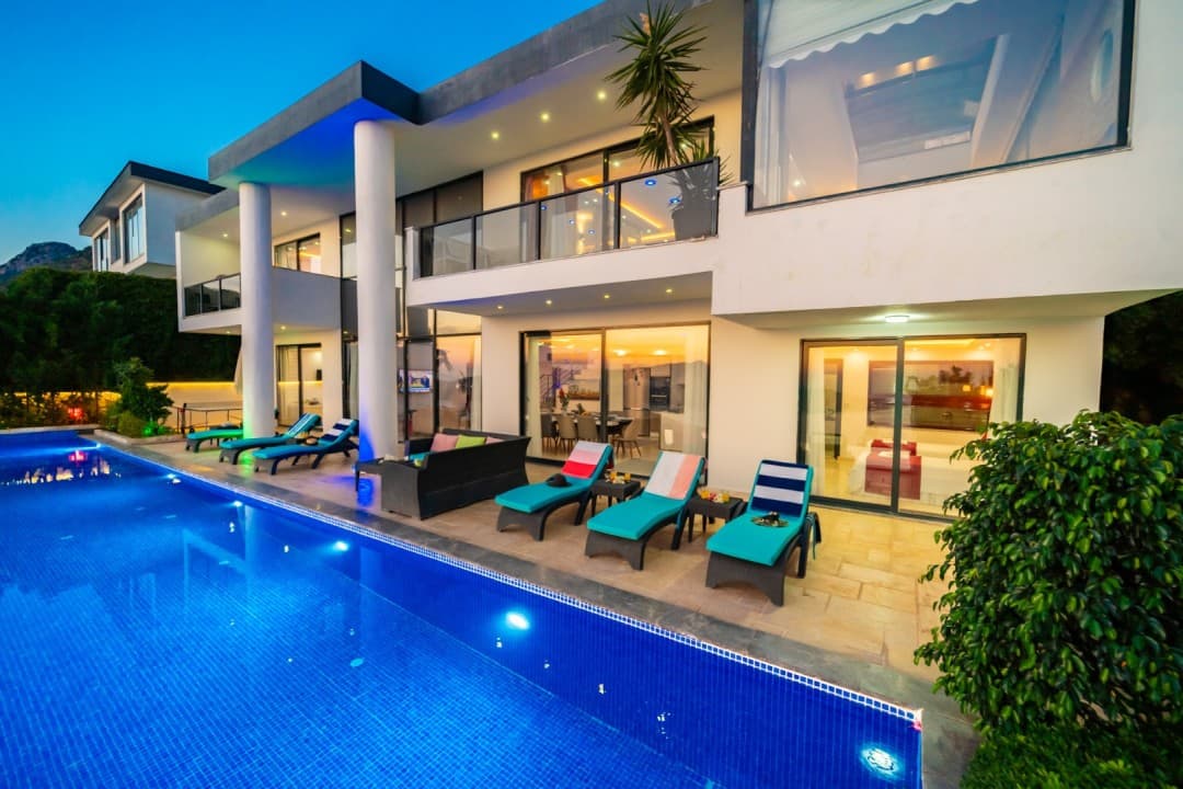 Akşam saatlerinde aydınlatılmış havuzu, şezlongları ve modern mimarisiyle iki katlı lüks villa.