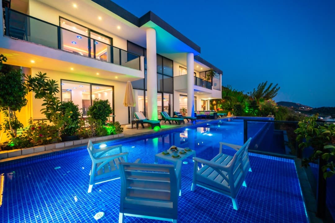 Akşam aydınlatmalı havuz ve oturma grubu önünde modern villanın dış cephesi.