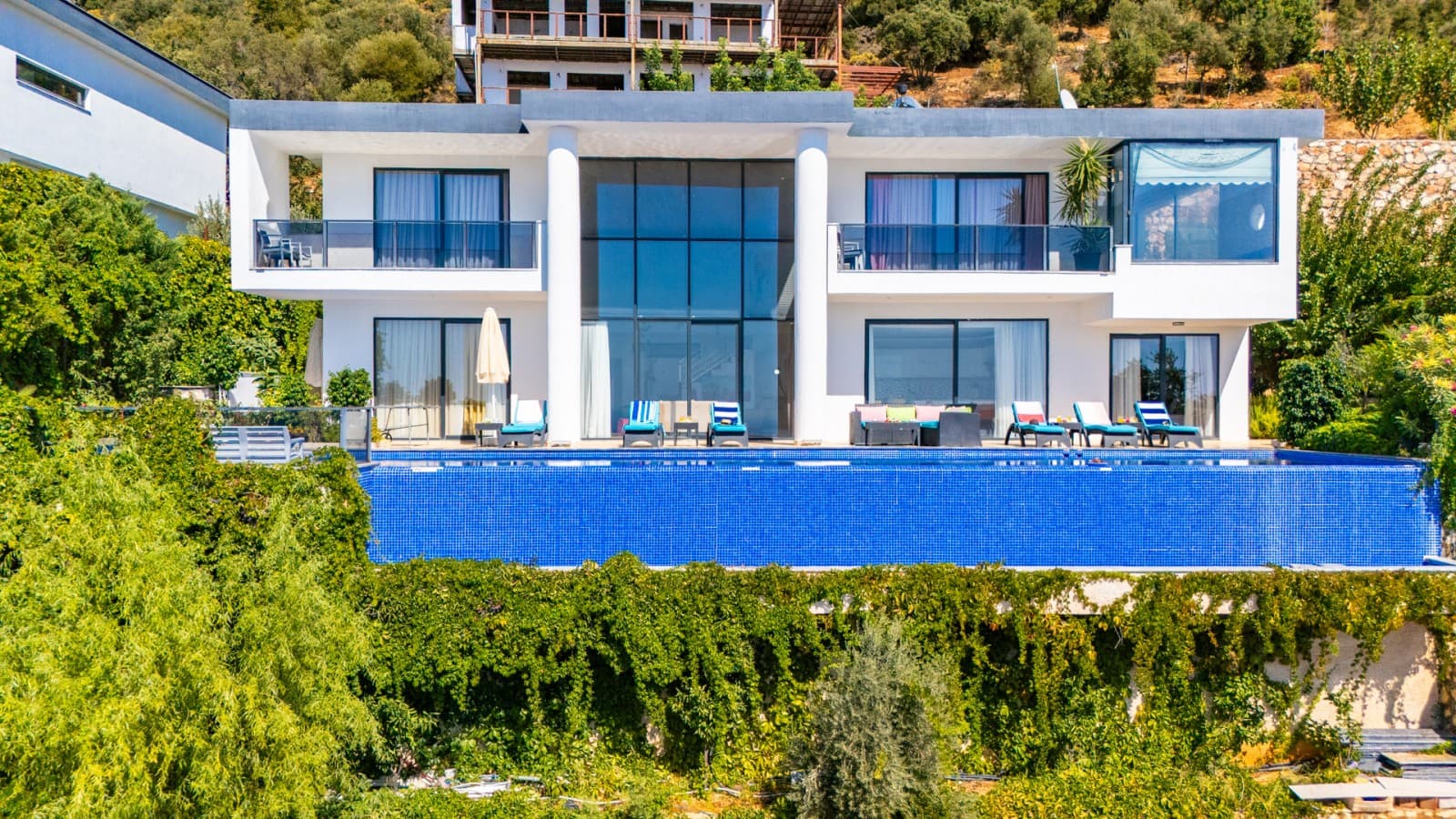 Geniş havuzlu ve iki katlı modern villanın ön cepheden görünümü.
