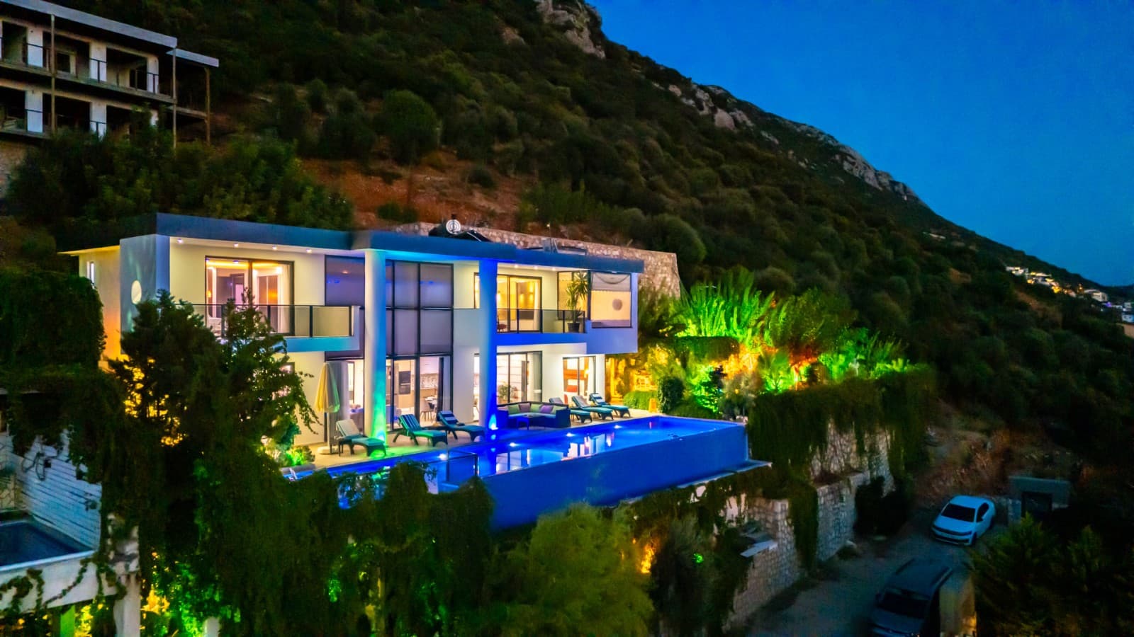 Akşam ışıklandırmalı, havuzlu ve dağ yamacında yer alan modern villa.