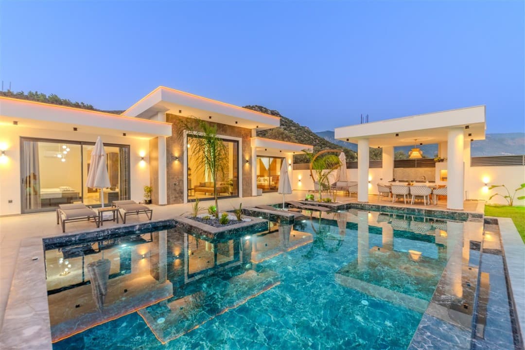 Alacakaranlıkta havuzlu modern villanın dış cephesi ve oturma alanı.