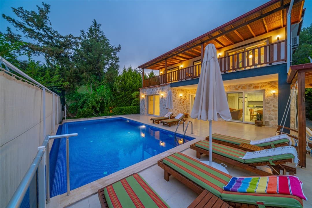 Akşam vakti aydınlatmalı havuz ve şezlongların bulunduğu iki katlı taş villa.