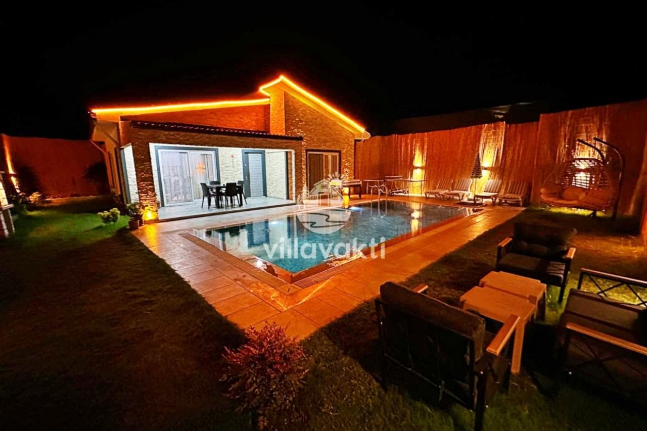 Aydınlatmalı villanın gece vakti havuz ve bahçe görünümü.