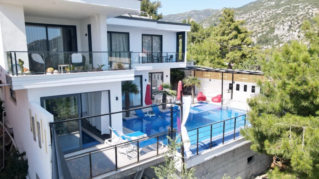 Bahçesinde havuz ve şezlonglar bulunan beyaz iki katlı lüks villa.