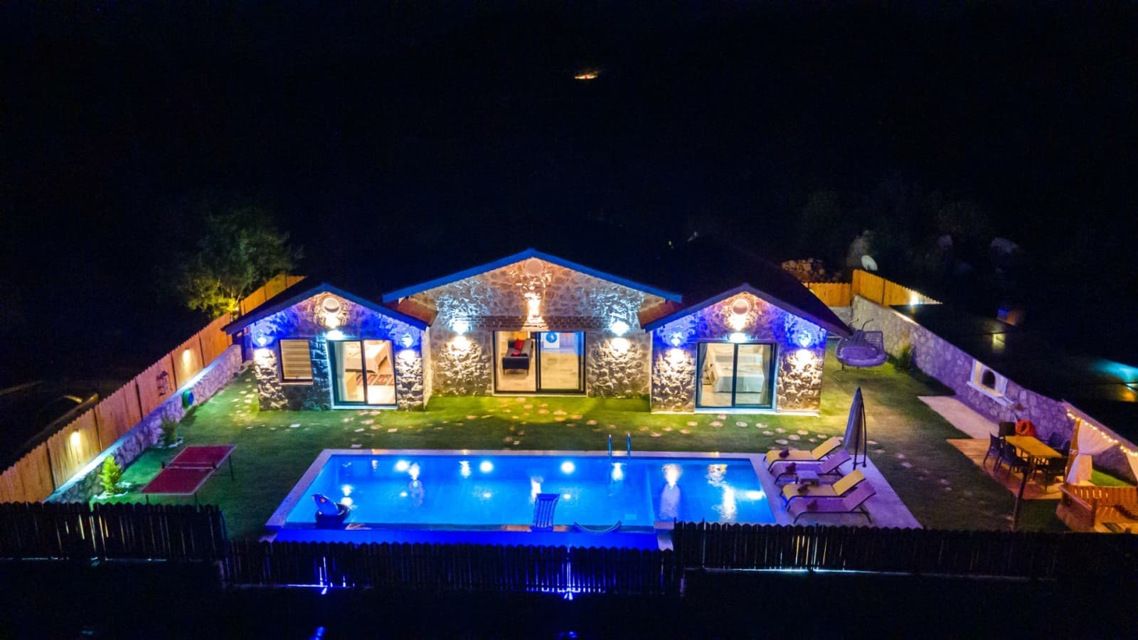 Gece aydınlatılmış taş cepheli müstakil villa ve önündeki havuz.