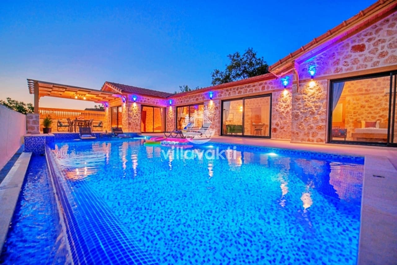 Akşam aydınlatmalı taş villa ve önünde büyük yüzme havuzu.