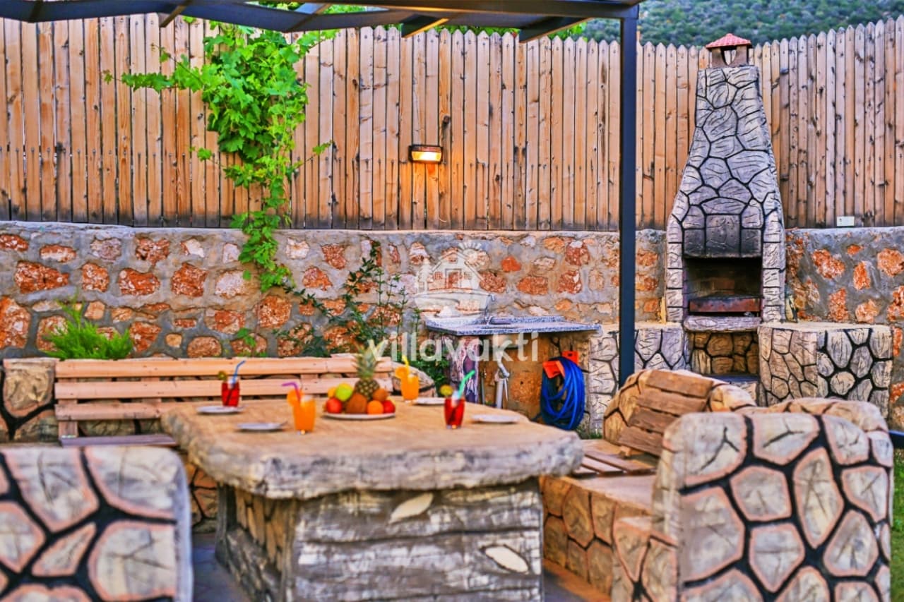 Bahçede taş masalı oturma alanı ve taş şömineli barbekü köşesi.