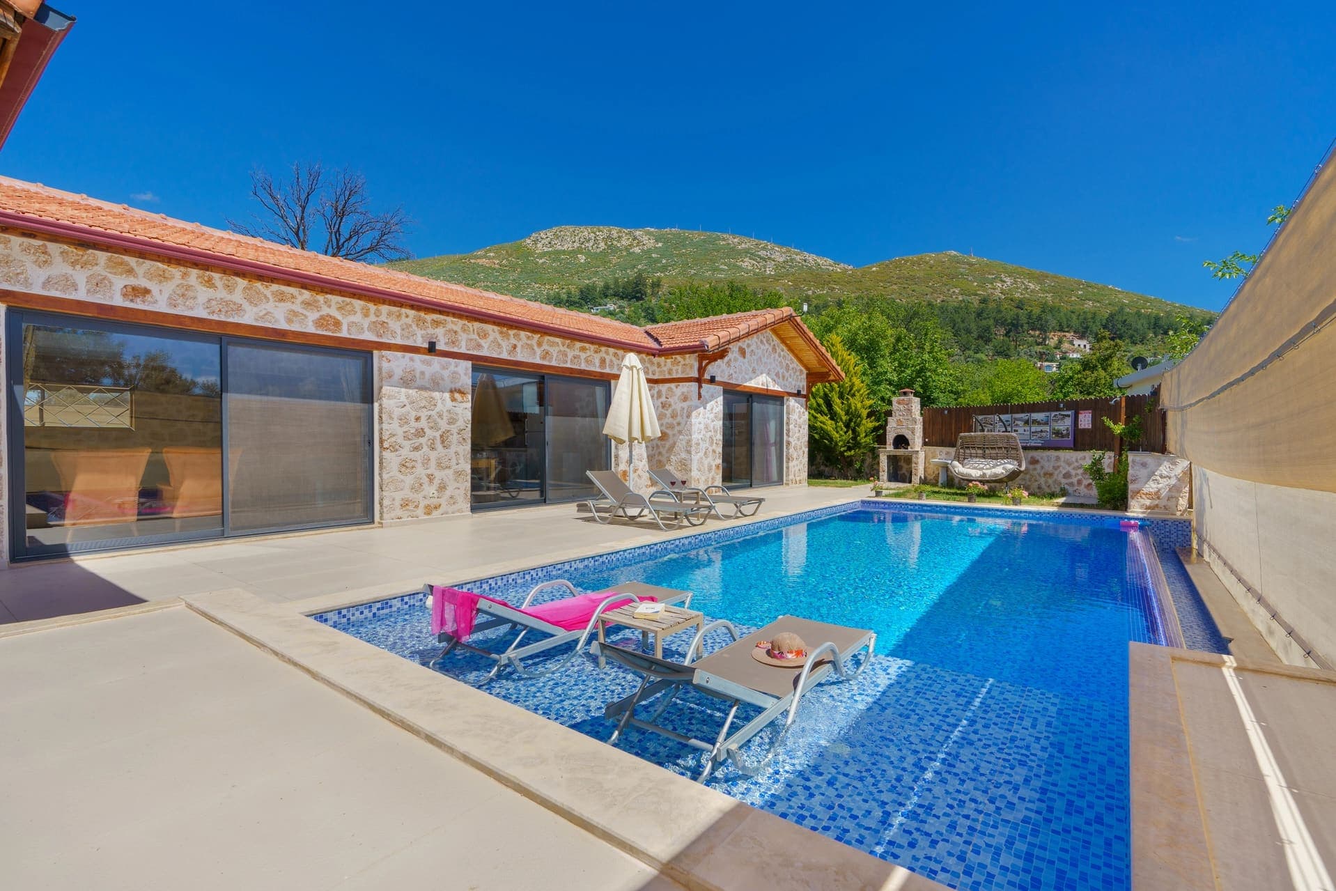 Açık havuzlu, taş cepheli villa ve dağ manzarası.
