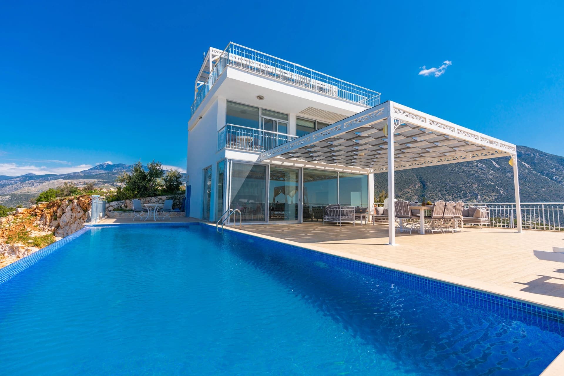 Havuz kenarında şezlonglar ve gölgelikli oturma alanı olan modern beyaz villa.