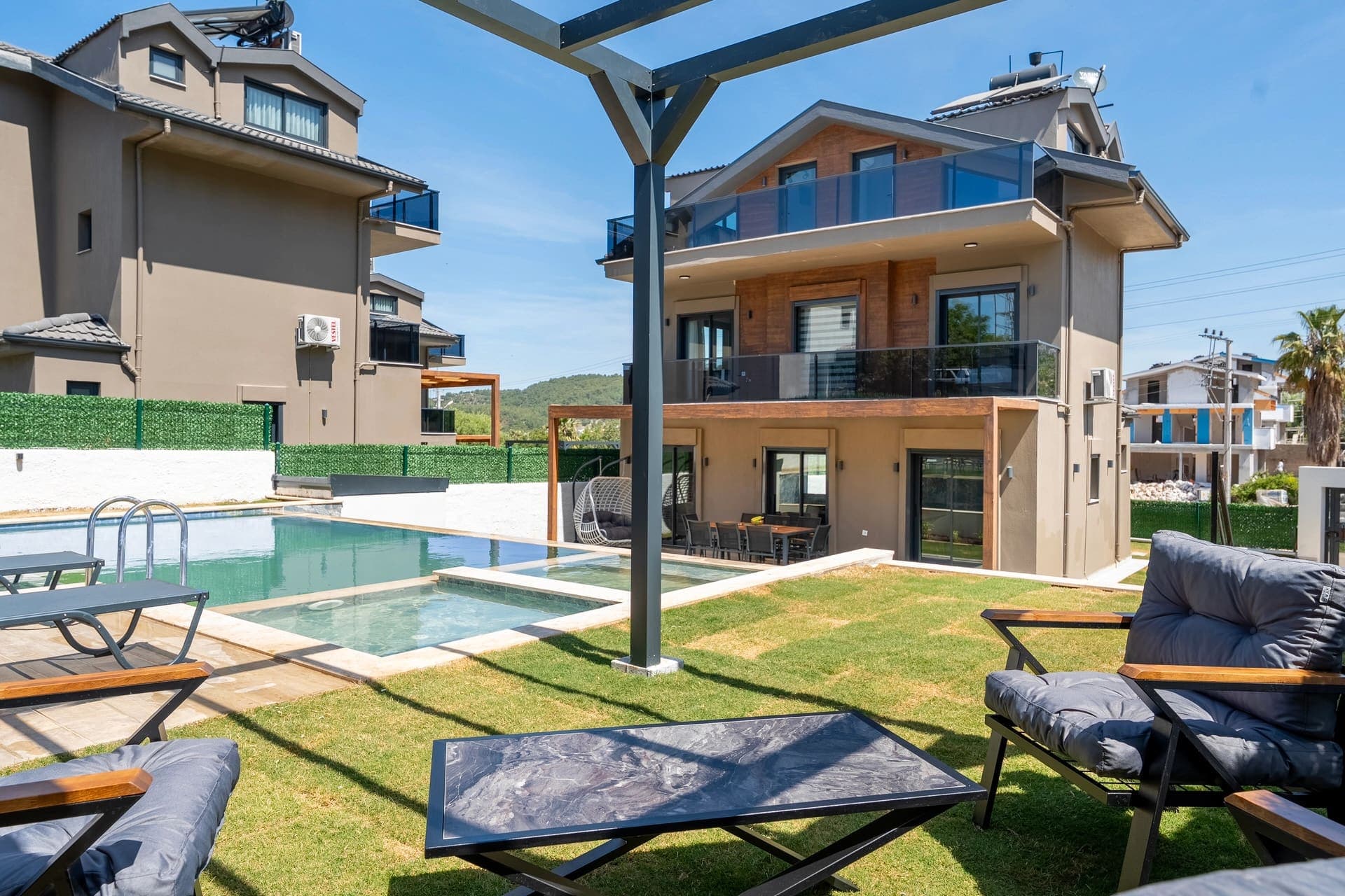 Gündüz vakti bahçeli, havuzlu lüks villa dış cephesi ve oturma alanı.