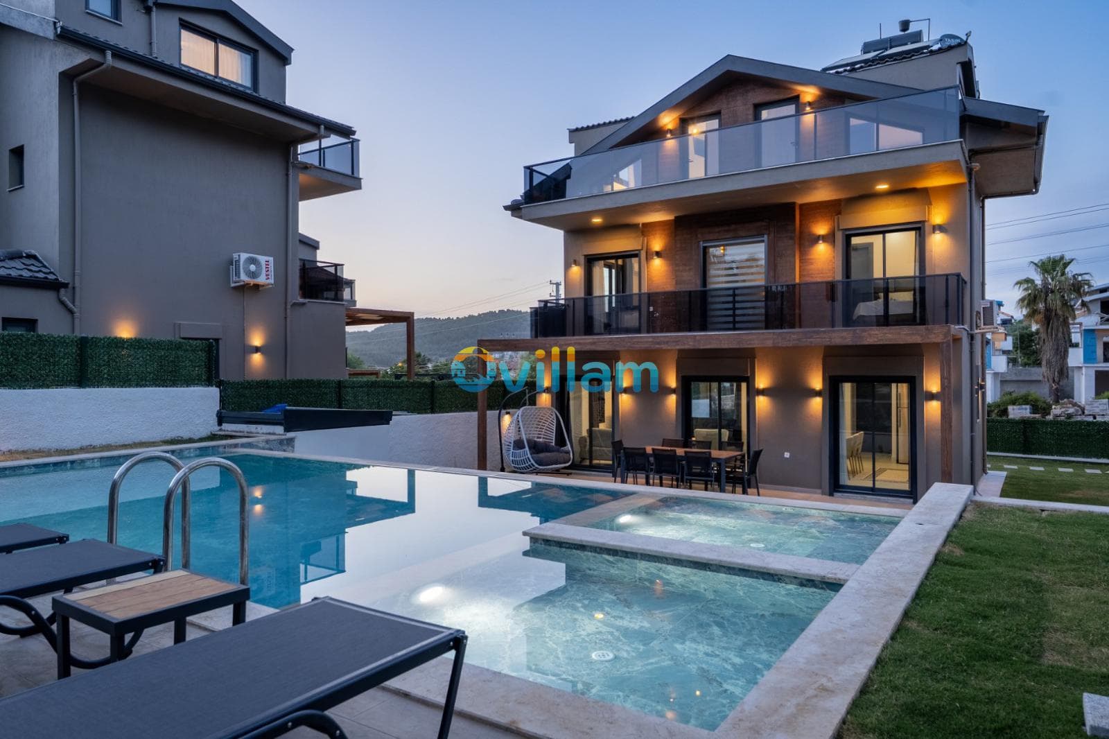 Akşamüstü aydınlatmalı villa dış cephesi ve havuz başı oturma alanı.