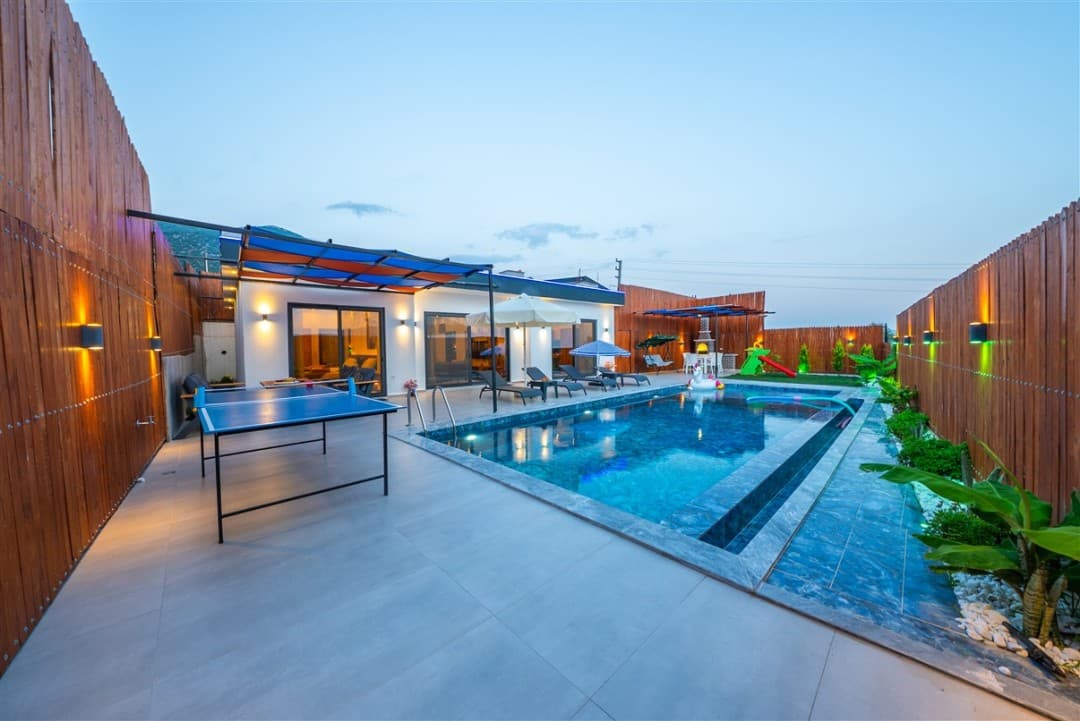 Ahşap çitlerle çevrili bahçesinde havuz, şezlonglar ve masa tenisi olan tek katlı villa.
