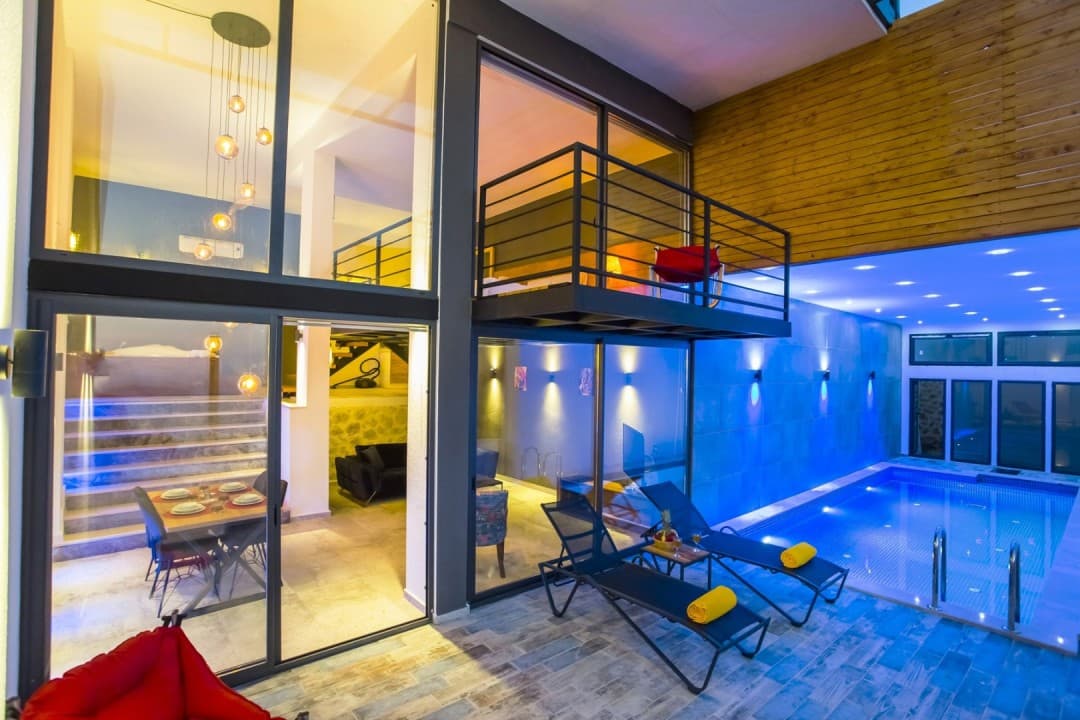 İç havuzlu modern villanın cam cepheli oturma alanı ve üst kat balkonu.