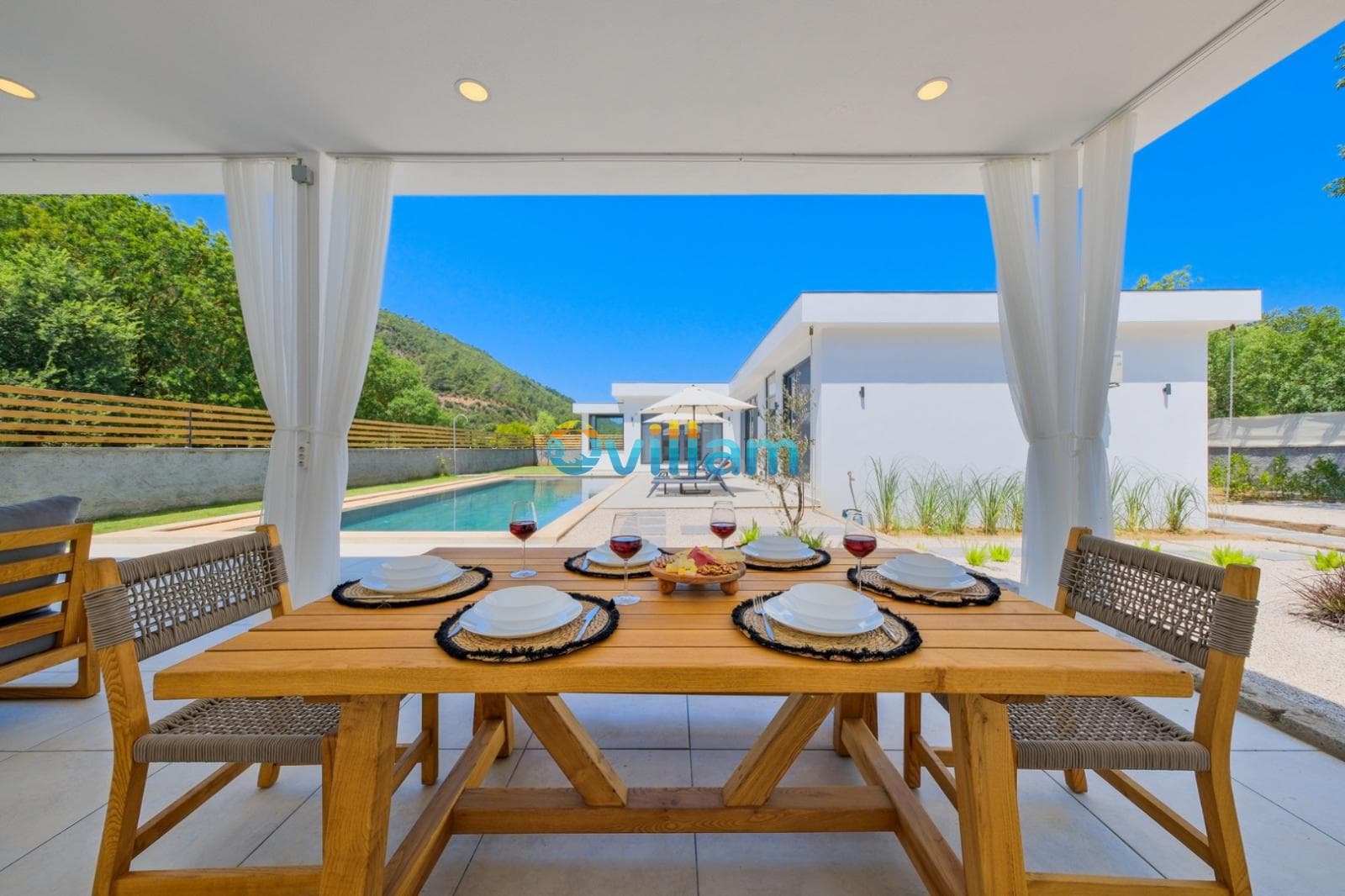 Havuz manzaralı verandada ahşap yemek masası ve servis takımları.
