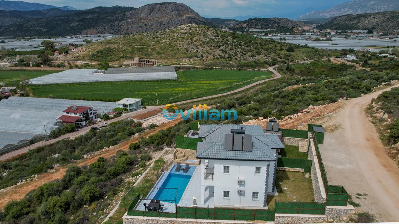 Dağ ve sera manzaralı yeşil doğa içinde konumlanan iki katlı beyaz villa.