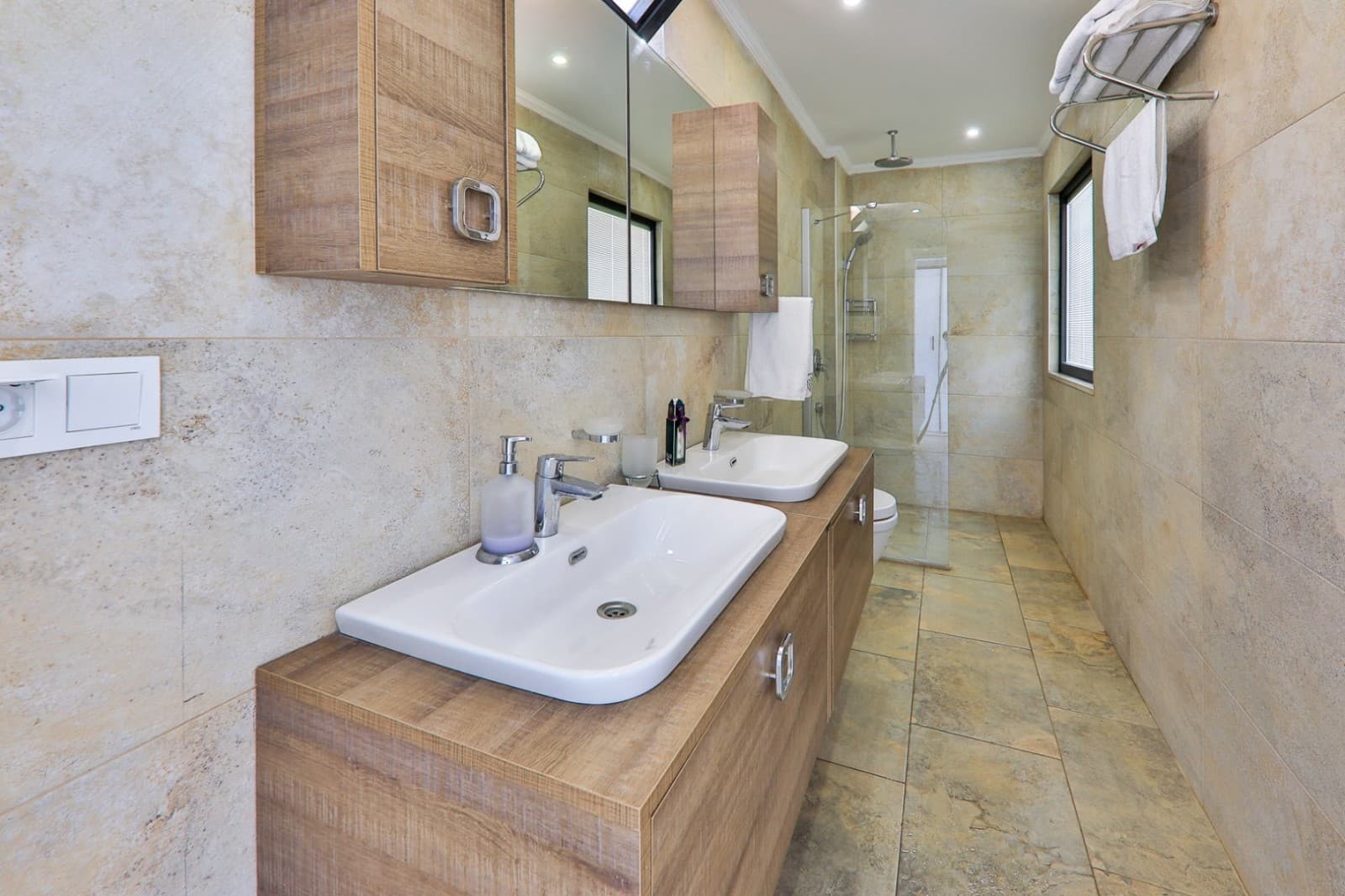 Ahşap dolaplı, çift lavabolu ve duşakabinli modern banyo.