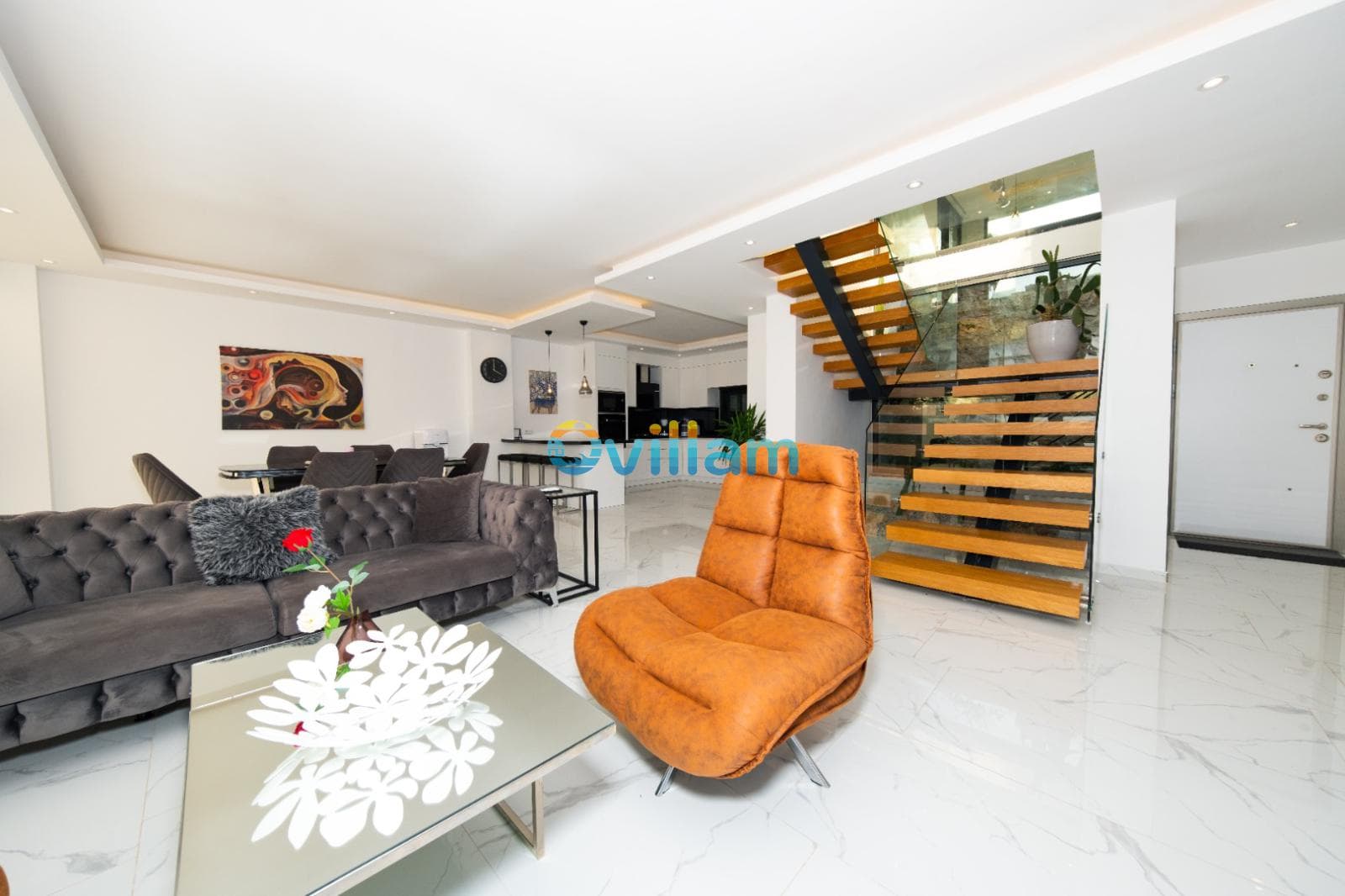 Açık renk mermer zeminli geniş salon, ahşap merdivenler ve modern oturma grubu.