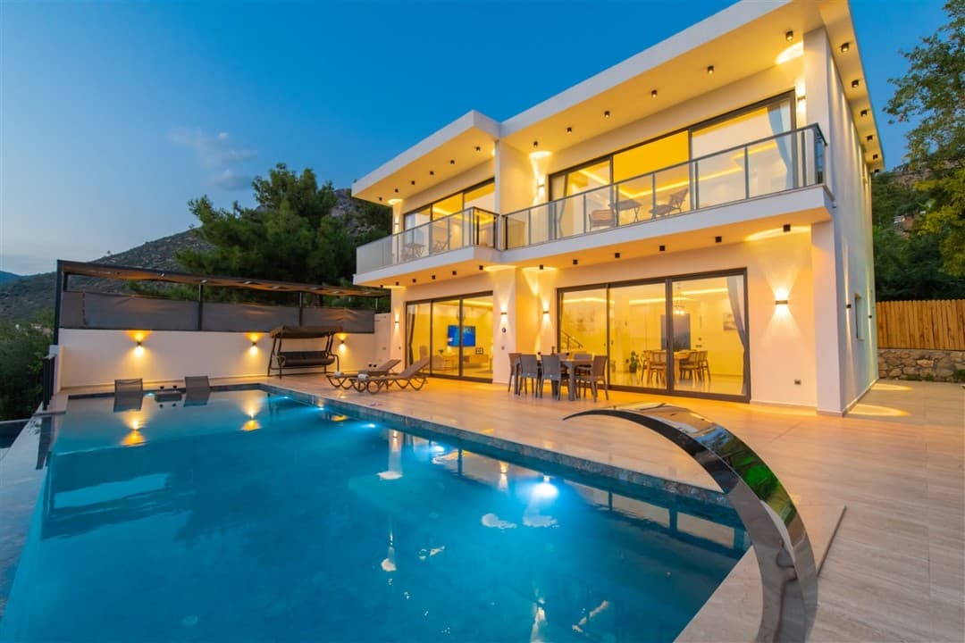 Alacakaranlıkta havuzu, şezlongları ve aydınlatılmış iki katlı modern villa.
