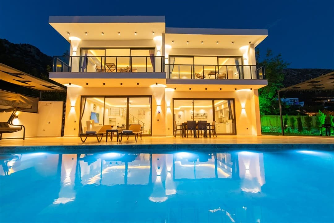 Gece ışıklandırılmış iki katlı villanın havuzlu dış cephesi.