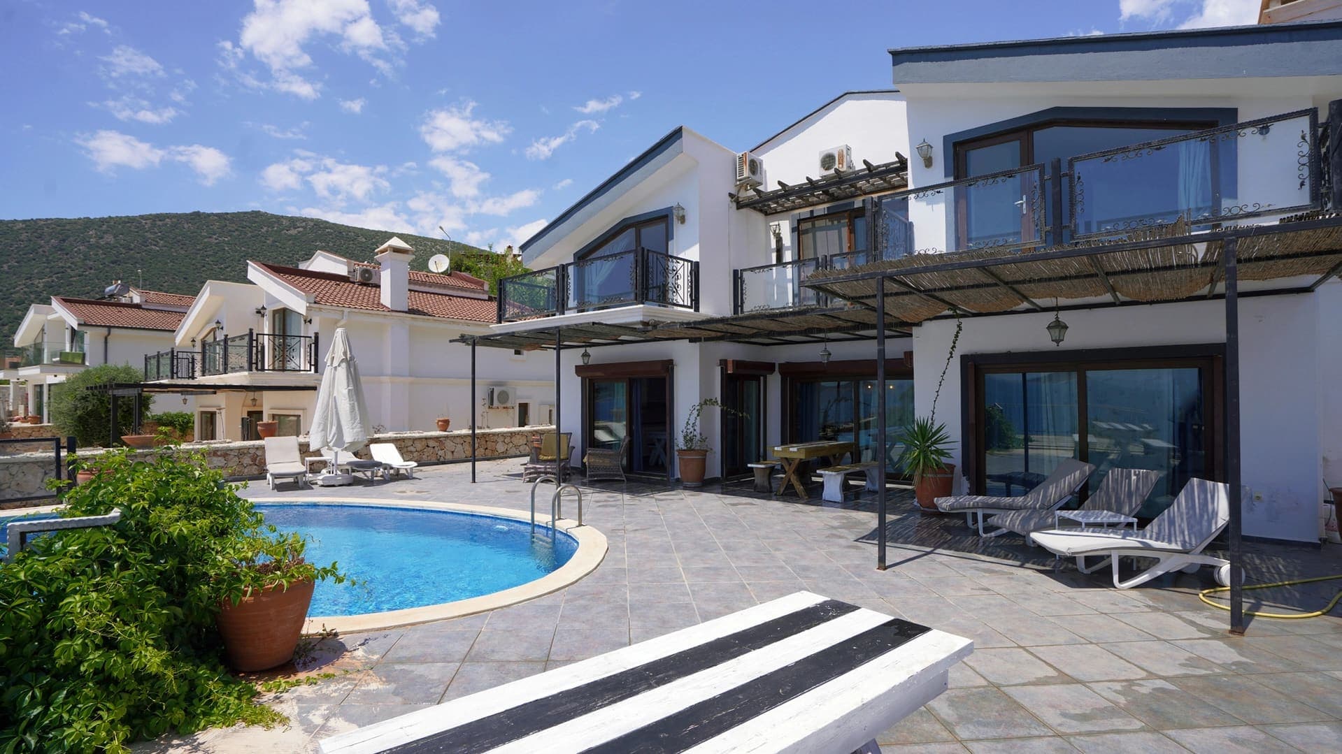 Havuz başında şezlonglar ve masa sandalyeler bulunan beyaz dış cepheli villa.
