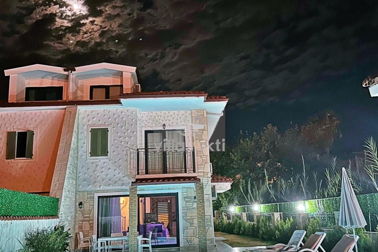 Gece vakti bulutlu gökyüzü altında aydınlatılmış iki katlı villanın dış cephesi.