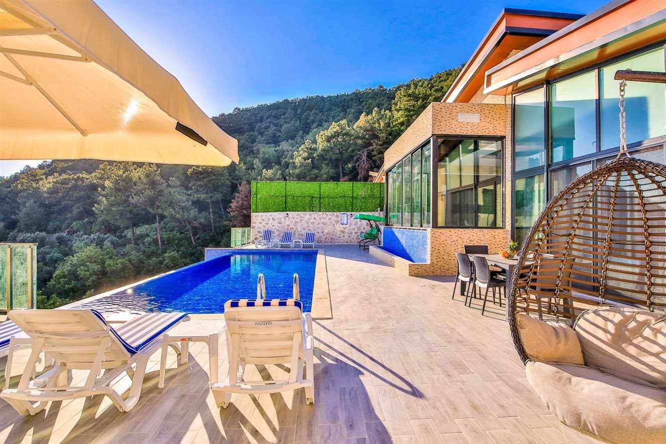 Orman manzaralı havuz başında şezlonglar, şemsiye ve oturma alanı bulunan villa terası.