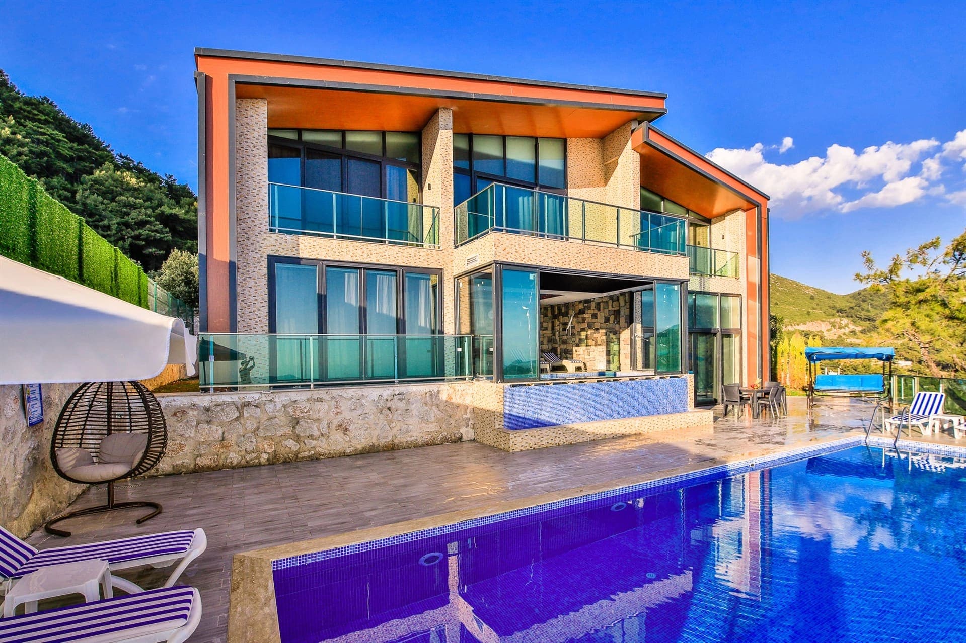 İki katlı, geniş cam balkonlu modern villanın önünde yüzme havuzu.