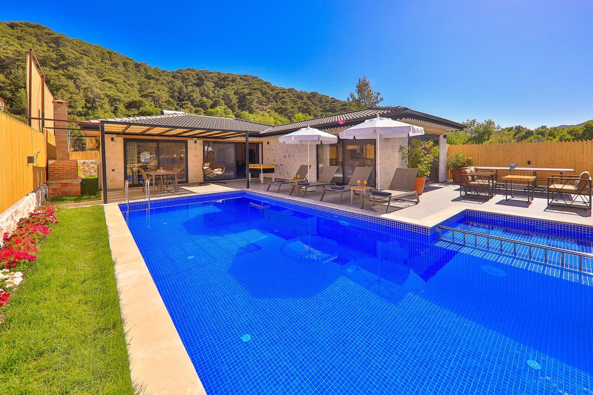 Mavi havuzun etrafında şezlonglar ve şemsiyeler bulunan müstakil villa bahçesi.