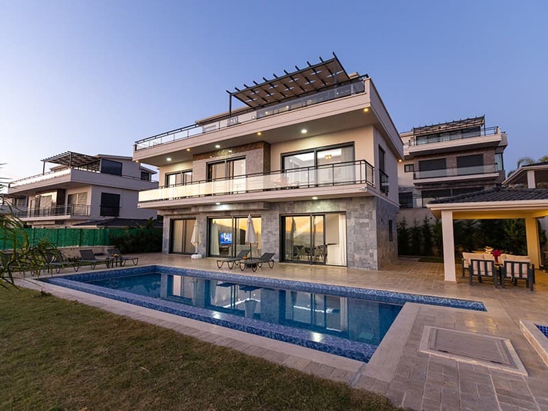 Akşam vakti aydınlatılmış, özel havuzlu ve teraslı modern mimariye sahip üç katlı villa.