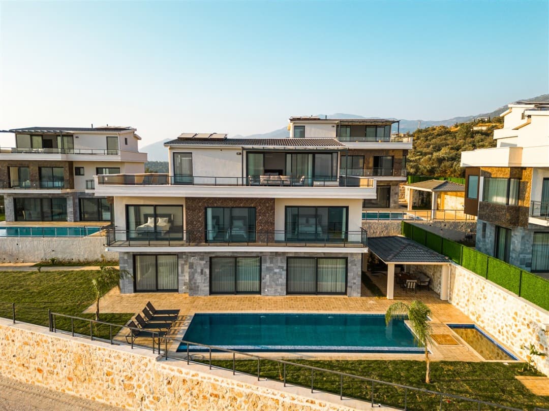 Önünde havuz bulunan modern ve çok katlı beyaz villanın dış cephe görünümü.