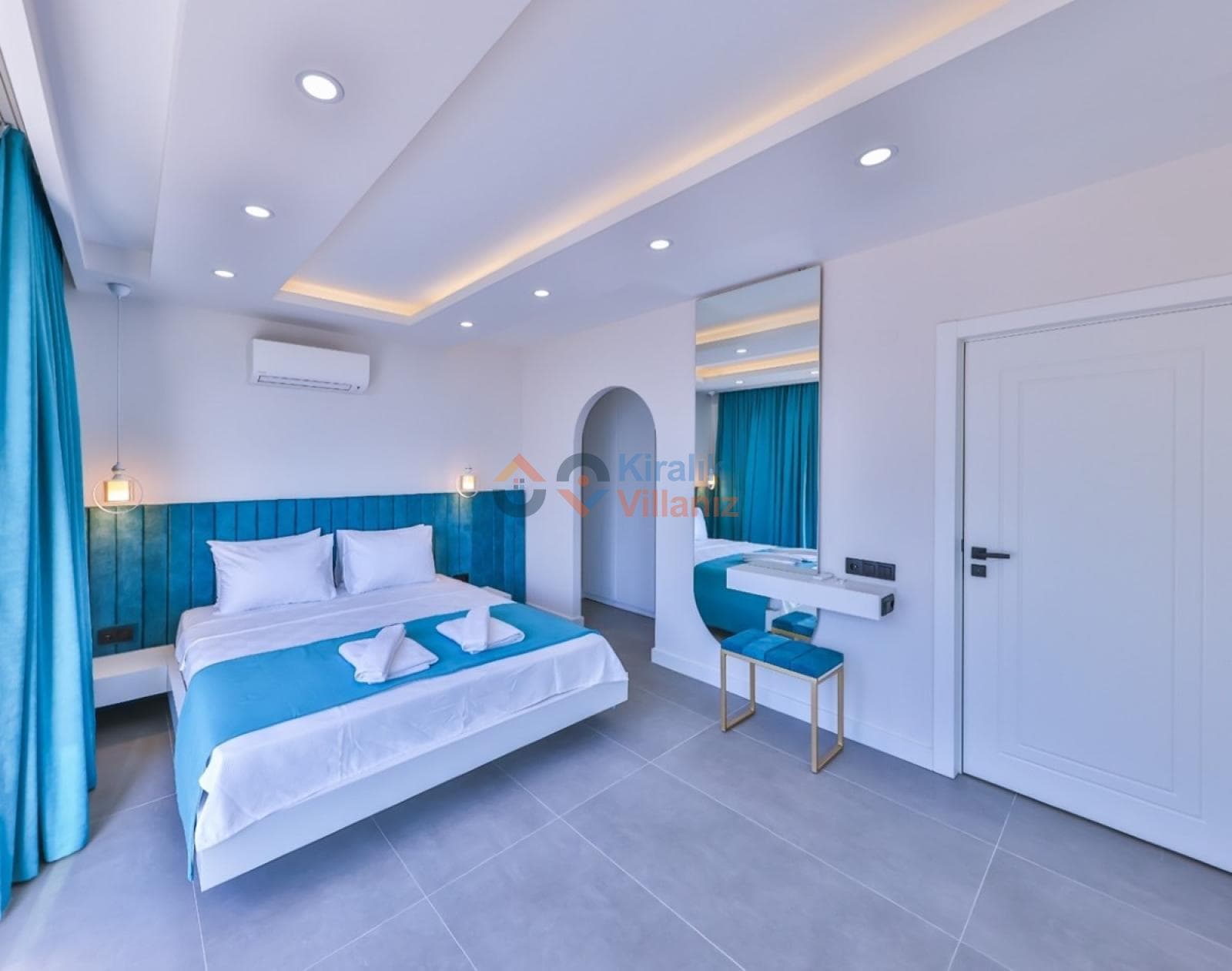 Mavi detaylı modern yatak odasında çift kişilik yatak ve makyaj masası bulunuyor.