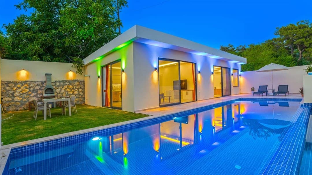 Akşam vakti aydınlatmalı havuzu ve bahçesinde yemek masası olan müstakil tek katlı villa.
