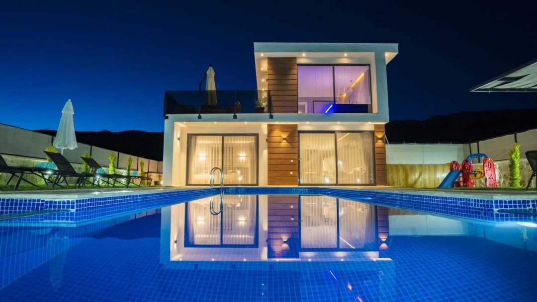 Aydınlatmalı iki katlı modern villa ve önünde havuz.