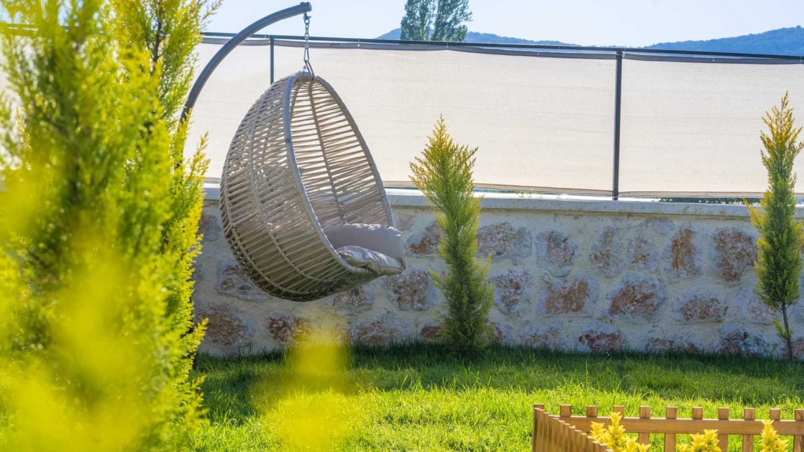 Bahçede yeşil ağaçlar arasında asılı bej renkli salıncak.