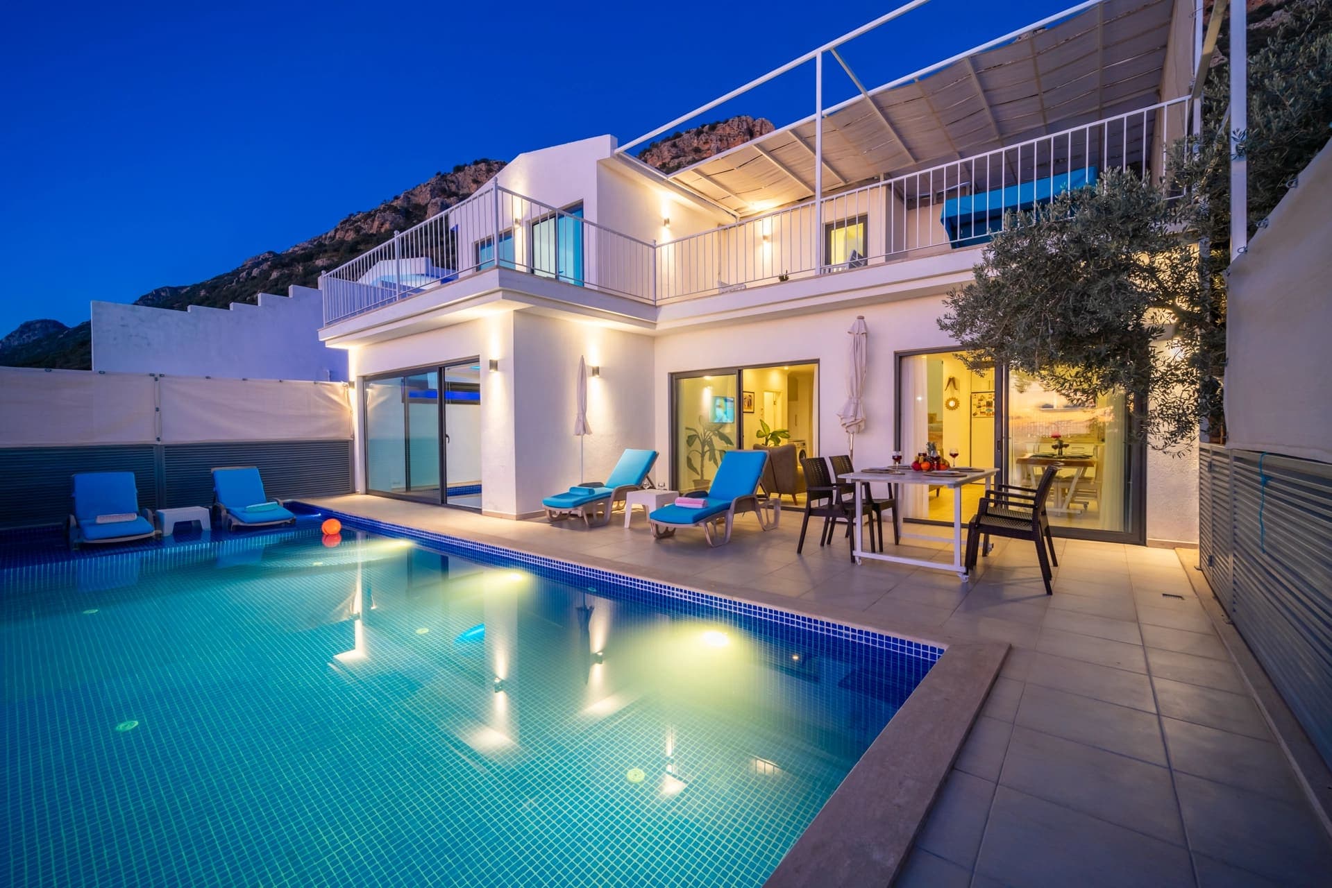 Akşam vakti aydınlatılmış havuzlu ve teraslı iki katlı beyaz villa.