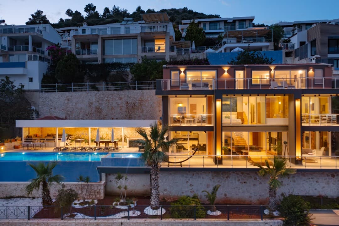 Gece ışıklandırılmış geniş havuzu ve terasları olan lüks villa dış cephesi.