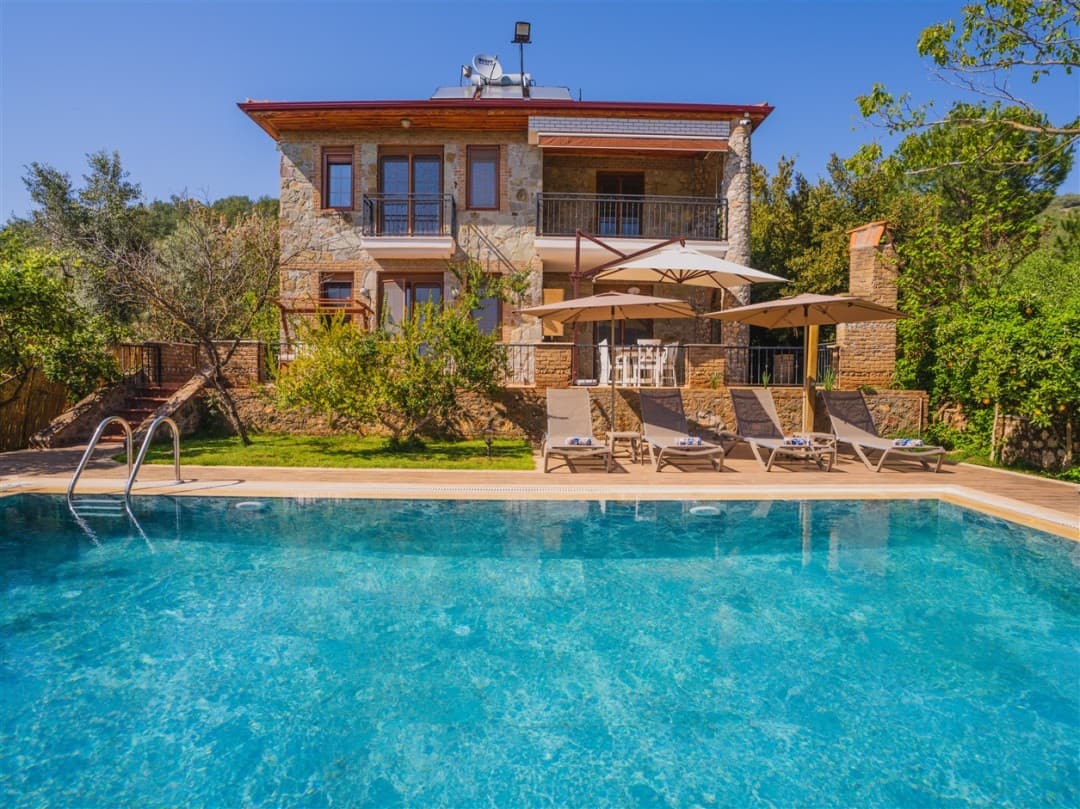 Taş duvarlı villa, havuz ve şezlonglar.