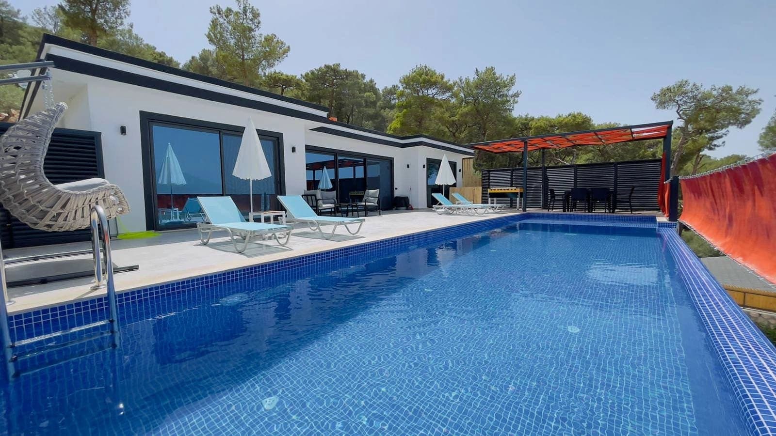 Orman manzaralı havuz kenarında şezlonglar ve salıncak bulunan villa bahçesi