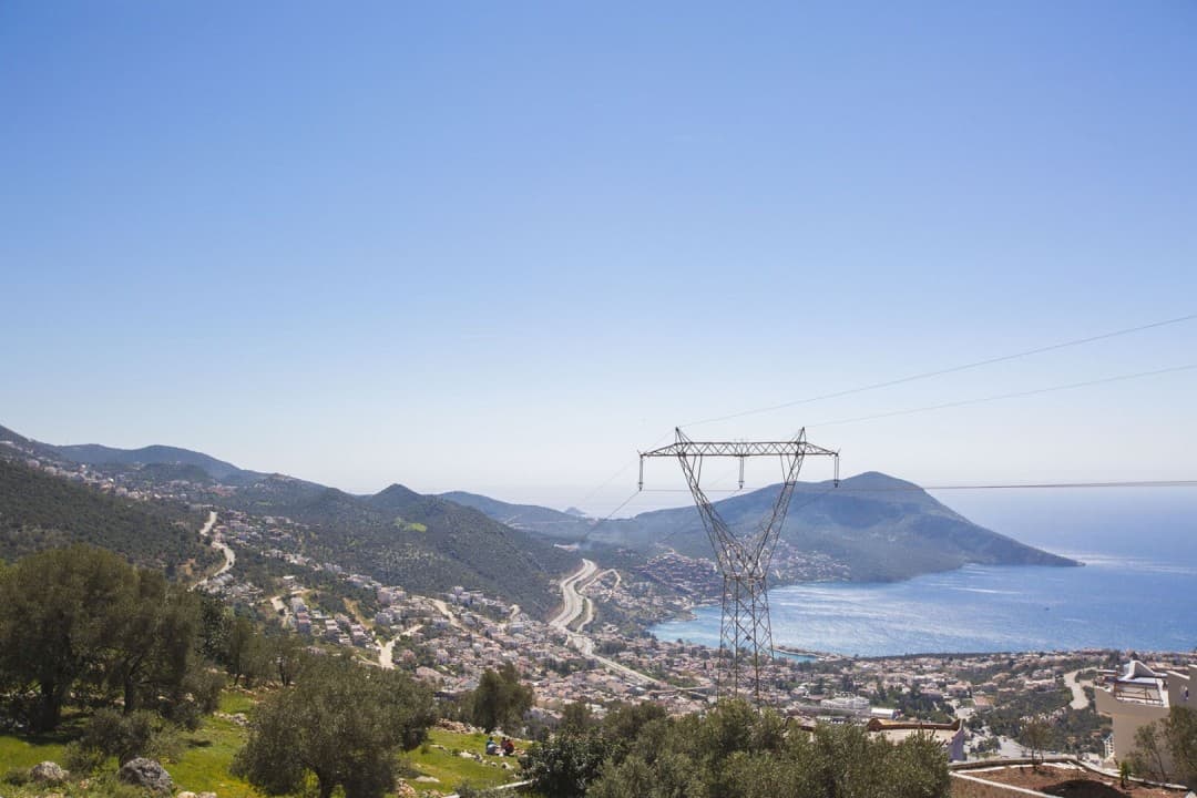 Deniz manzaralı bir koy, yamaçtaki yerleşim yeri, kıvrımlı yollar ve yüksek gerilim hattı direği.