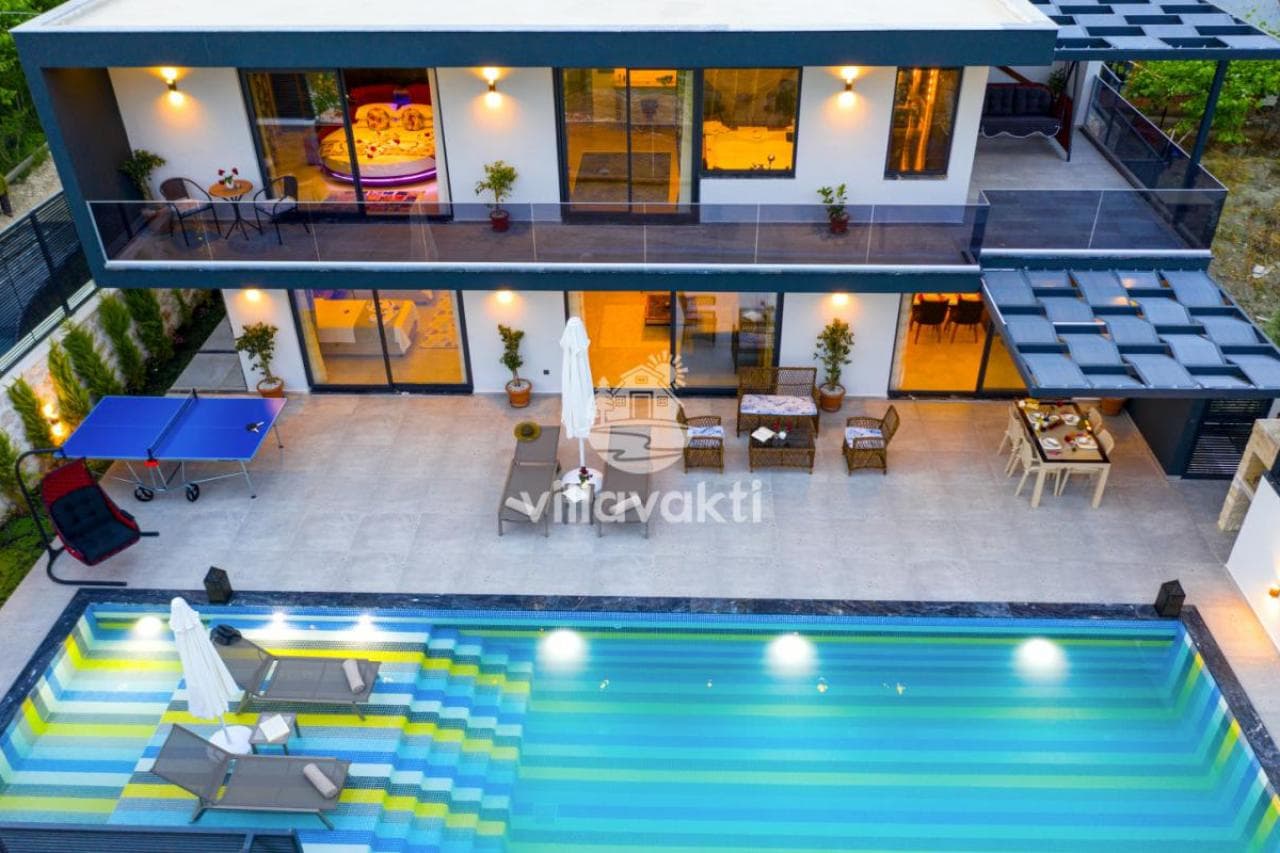 Aydınlatmalı havuzu ve şezlongları olan iki katlı modern villanın dış cephesi