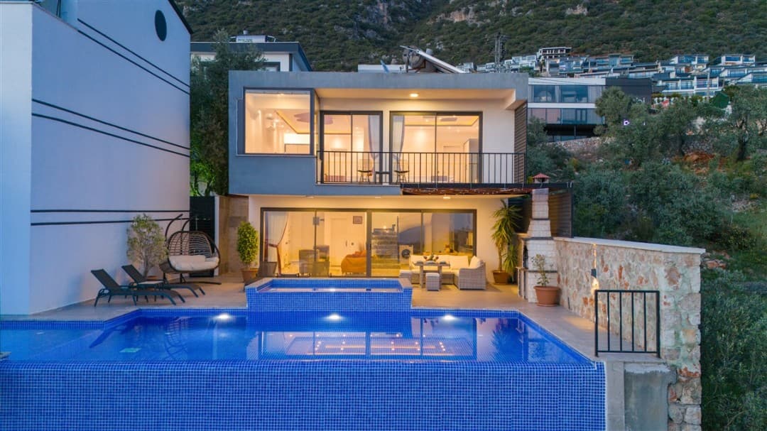 Akşam ışıklarıyla aydınlanan, özel havuzlu, iki katlı modern villanın dış cephesi ve bahçesi.