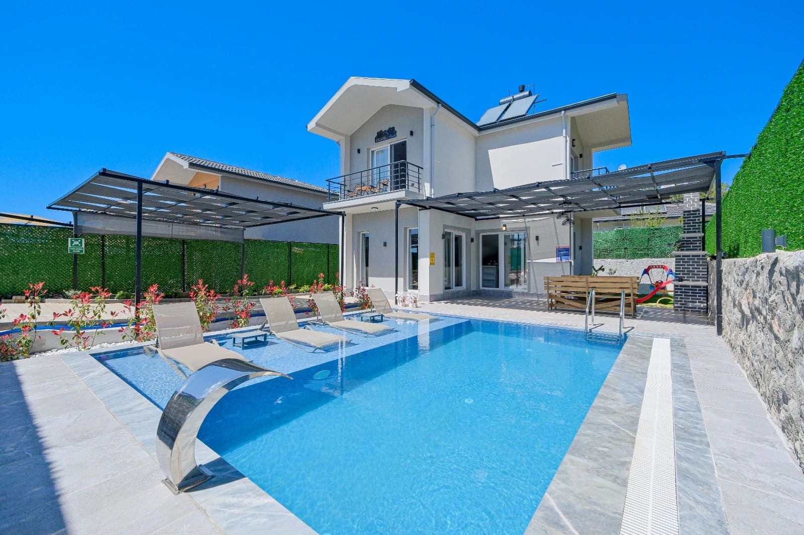 Geniş yüzme havuzu ve şezlongların bulunduğu iki katlı villa dış cephesi.