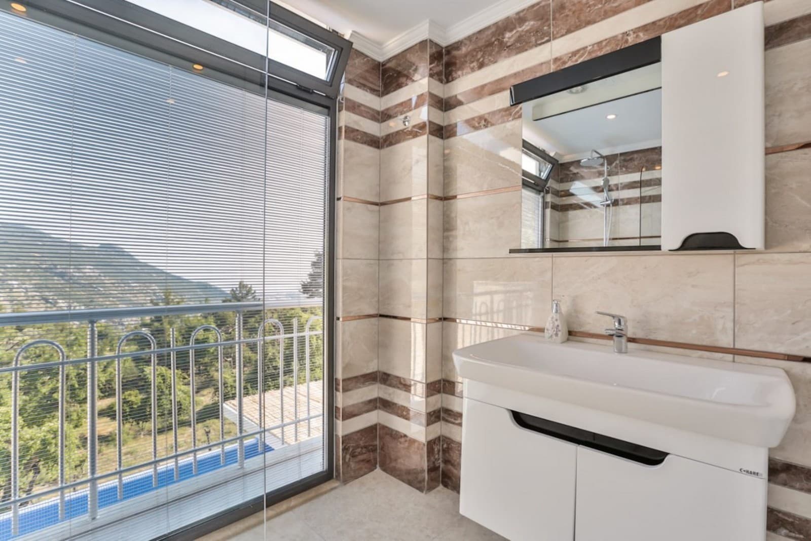 Bej mermer kaplı banyoda lavabo, ayna ve manzaralı pencere.