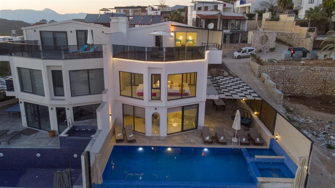 Gündüz çekiminde, önünde havuz ve şezlonglar bulunan beyaz cepheli modern villanın genel görünümü.