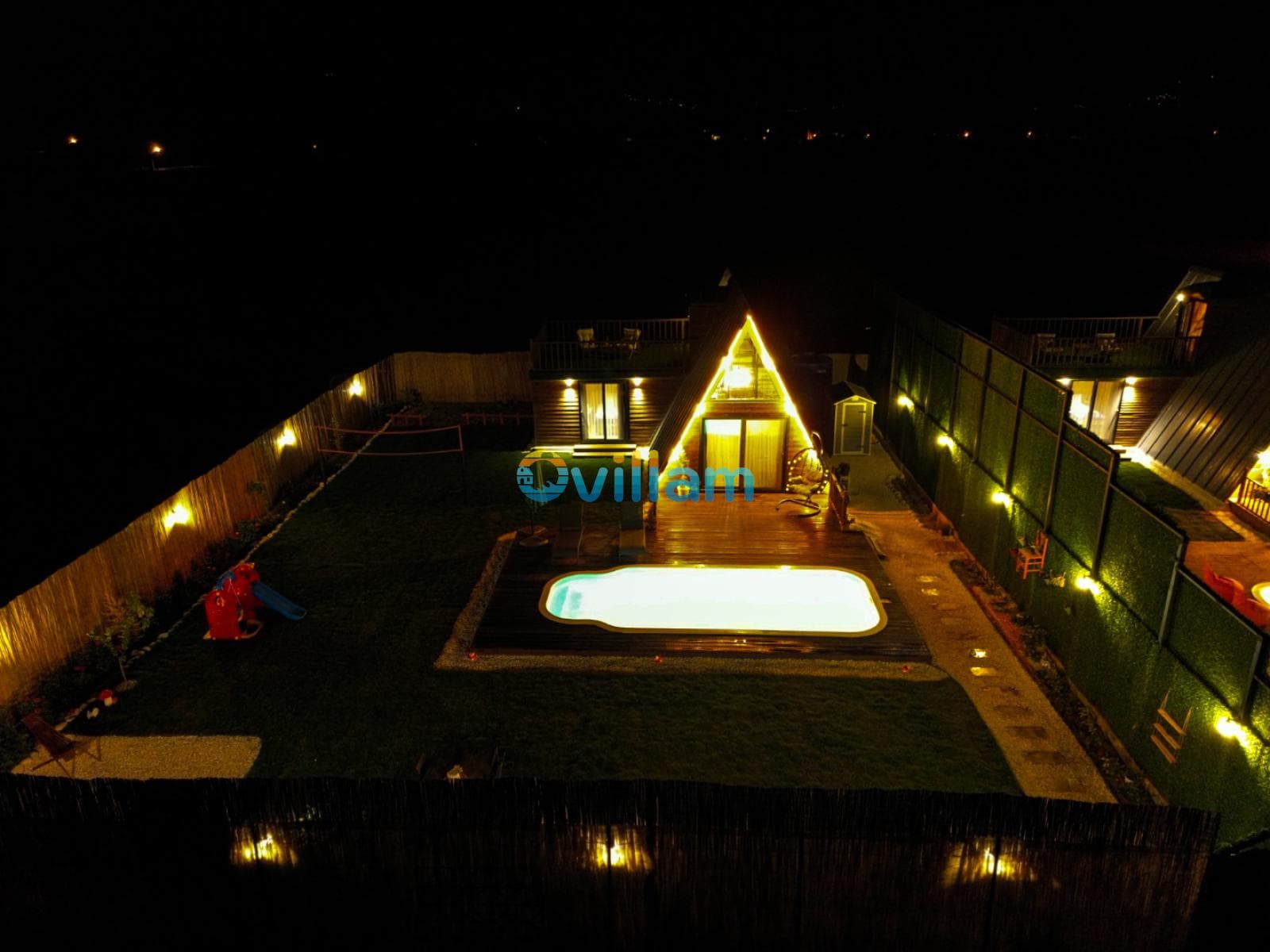 Gece vaktinde havuzu aydınlatılmış villa ve bahçesi.