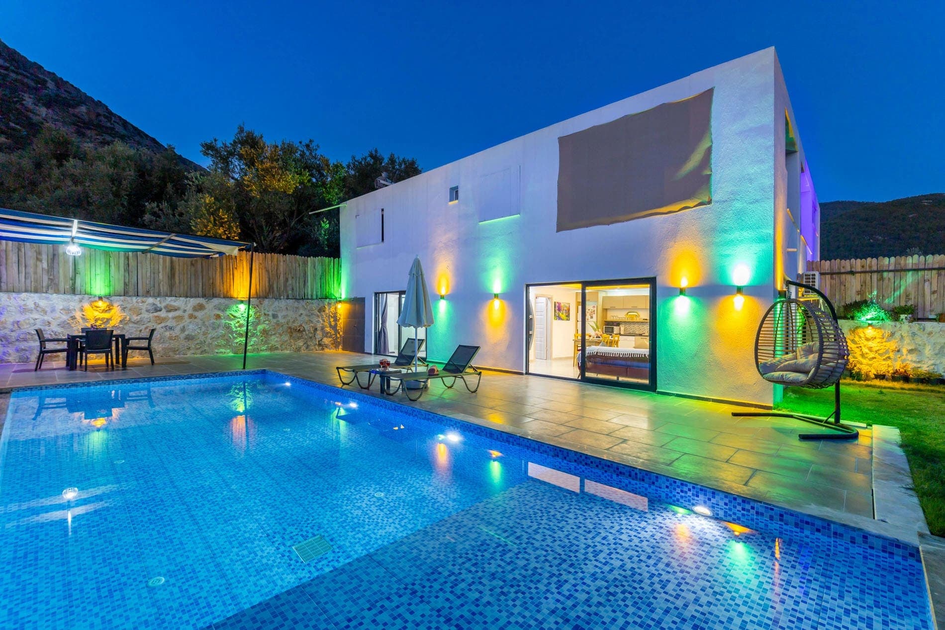 Akşam aydınlatmalı havuz ve bahçeye bakan iki katlı beyaz villa